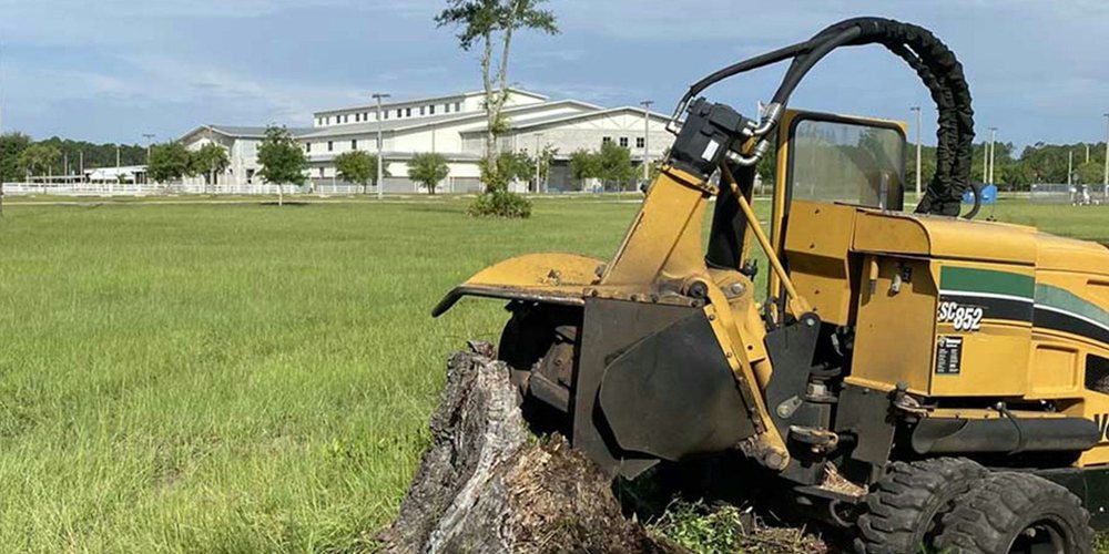 A tracked stump grinder positioned over a large stump in a grassy yard
